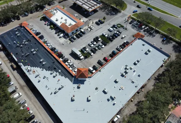 A drone view of a shopping plaza mid-installation, half the roof stripped to the deck and half already covered in new white membrane.