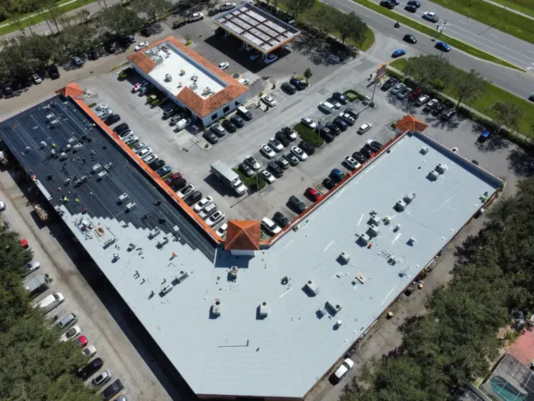 A drone view of a finished white commercial roof over a retail plaza and its car park.