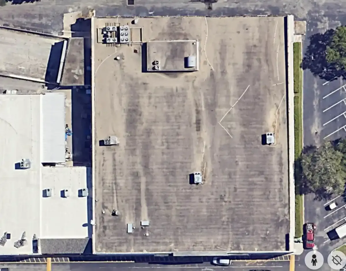 A retail plaza roof from directly overhead before coating, the deck weathered brown and streaked.