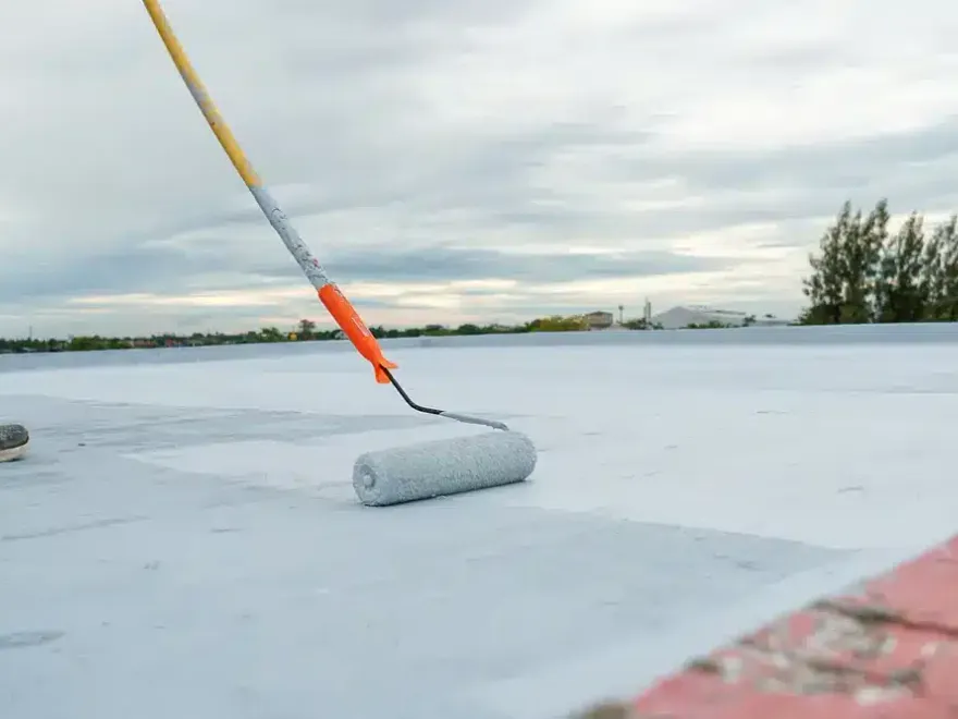 A roller on a pole laying white silicone coating across a flat roof.