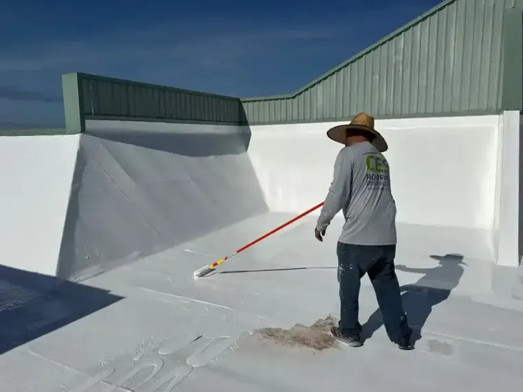 A CES crew member pushing a squeegee across a white coated roof.