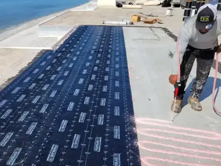 A CES crew member rolling out dark membrane across a beachfront commercial roof.
