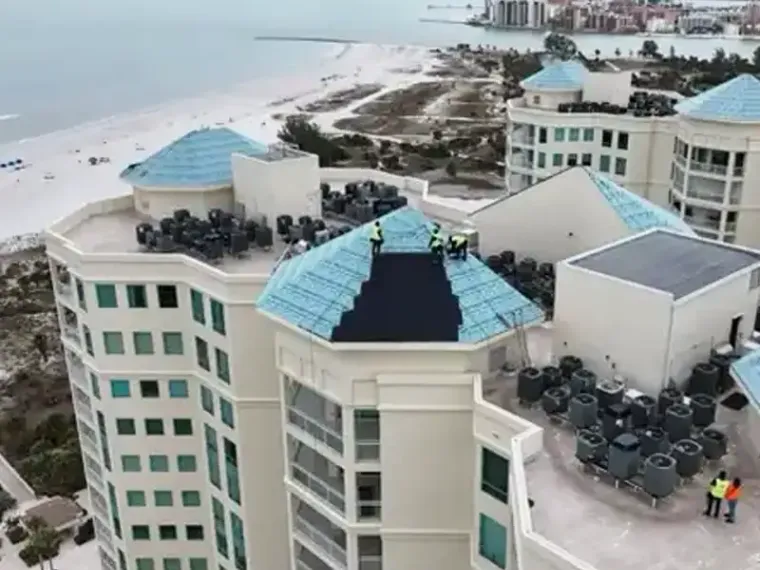 A drone view of a beachfront hotel complex with crews working on its roofs.