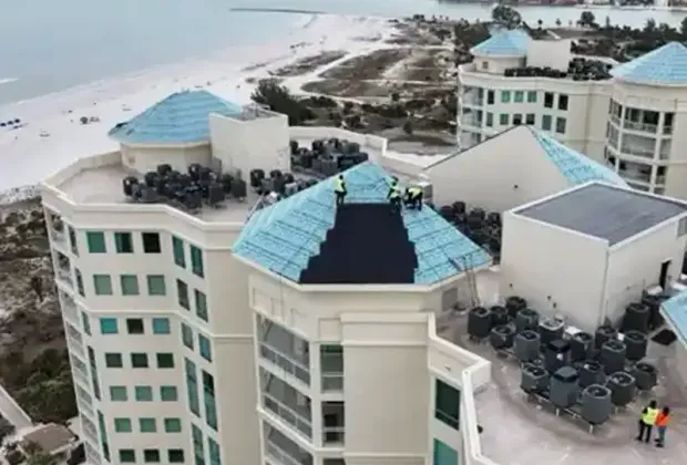 Crews in high-visibility vests working on the roof of a beachfront tower, new underlayment down over one section.